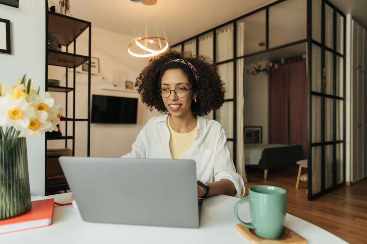 uma jovem sorrindo trabalhando home office em casa em frente um notebook