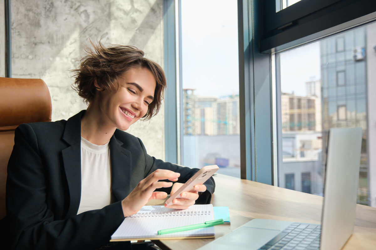 Funcionária feliz marcando ponto no celular em uma mesa de escritório